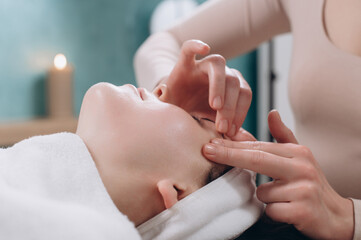 The beautician makes a deep facial massage to a young woman. Face massage technique against aging. Close-up.