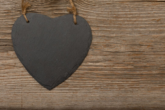 black slate heart with stripes on rustic brown wooden background with free space for text