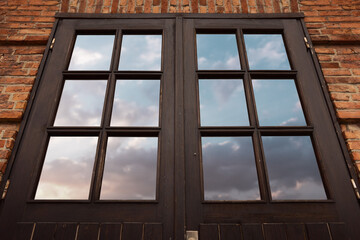 Vintage dark brow wooden doors with glass reflecting a blue sky.