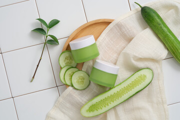 Two green jars without label are placed on a wooden dish with white towel and Cucumber slices....