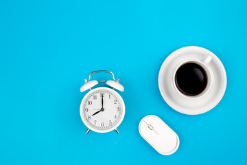 Alarm clock, computer mouse and a cup of coffee on a blue background, top view.