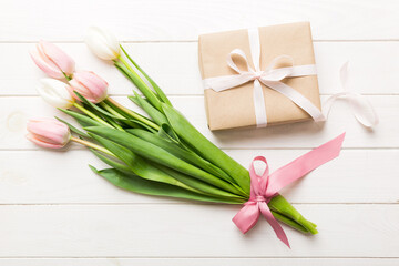 Fototapeta premium Pink tulips flowers and gift or present box on colored table background. Mothers Day, Birthday, Womens Day, celebration concept. Space for text top view