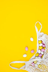 Colored Easter eggs in a mesh bag on a yellow background, flat lay.