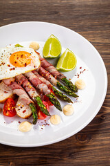 Sunny side up egg and asparagus wrapped in bacon on wooden background
