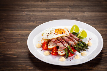 Sunny side up egg and asparagus wrapped in bacon on wooden background
