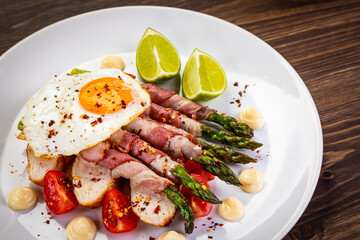 Sunny side up egg and asparagus wrapped in bacon on wooden background
