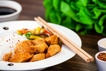 Asian food - chicken nuggets, rice noodles, stir fried vegetables, soy sauce and mushrooms on wooden table 