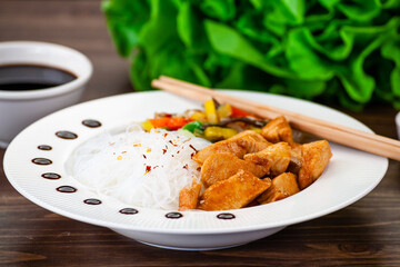 Asian food - chicken nuggets, rice noodles, stir fried vegetables, soy sauce and mushrooms on wooden table 
