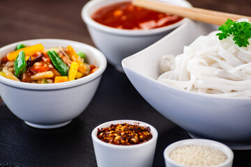 Asian food - chicken nuggets, rice noodles, stir fried vegetables, soy sauce and mushrooms on wooden table 