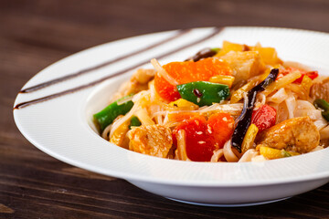 Asian food - chicken nuggets, rice noodles, stir fried vegetables, soy sauce and mushrooms on wooden table 