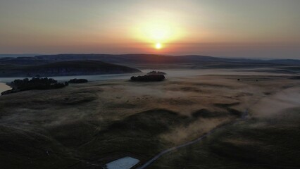 Obraz premium Beautiful sunset over the field and a river covered in fog.