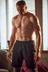 Obraz premium Image of handsome young man with muscular, beautiful relief body posing shirtless at home on day time. After training. Concept of sportive lifestyle, body and health care, fitness, health