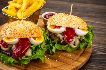 Big hamburgers with boiled egg and French fries on wooden board
