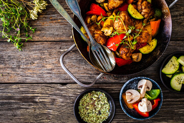 Fried chicken nuggets with vegetables in frying pan on wooden table
