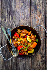 Fried chicken nuggets with vegetables in frying pan on wooden table
