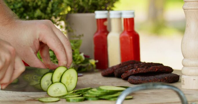Hands slicing cucumber with sharp Damascus steel knife preparing healthy vegan burger