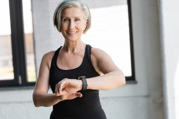 fit senior woman in black tank top smiling while checking activity on fitness tracker in gym.