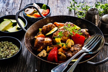 Fried chicken nuggets with vegetables in frying pan on wooden table
