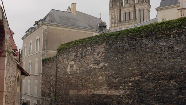 Pan shot of buildings alongside a street in the old town of Angers with main Cathedral in the background in France on a cloudy day.