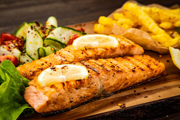 Fried salmon steak with French fries and fresh vegetable salad served on wooden table
