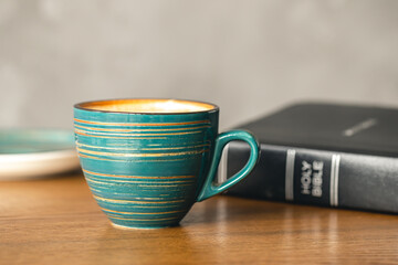 A cup of coffee and a Bible on a wooden table, close-up.
