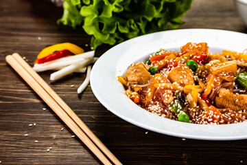 Asian food - chicken nuggets, rice noodles, stir fried vegetables, soy sauce and mushrooms on wooden table

