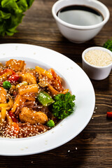 Asian food - chicken nuggets, rice noodles, stir fried vegetables, soy sauce and mushrooms on wooden table
