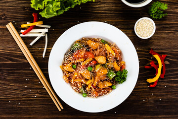 Asian food - chicken nuggets, rice noodles, stir fried vegetables, soy sauce and mushrooms on wooden table
