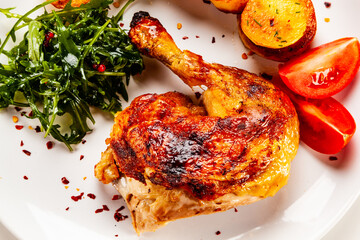 Barbecued chicken thigh with fried potatoes, arugula and tomatoes on white background