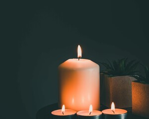Selective focus of a lightening big candle next to a small pot plant with gray background