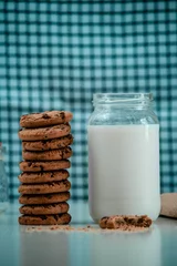 Gordijnen Closeup of tasty cookies with a jar of milk on the table on blue background © George Fallon/Wirestock Creators