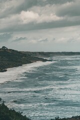 Vertical shot of the rocky shore and sea on a cloudy day.