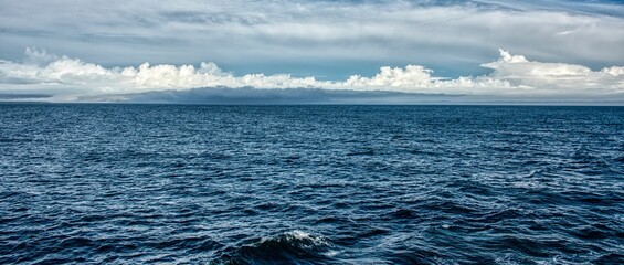 Naklejka premium Panoramic shot of a beautiful dark blue sea with cloudy sky in the background