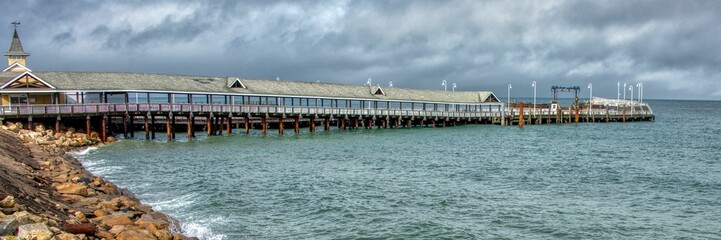 Panoramic shot of a coastal landscape with a long pier under a gloomy sky