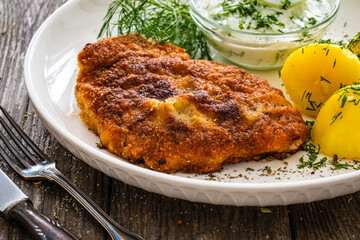 Breaded fried pork chop with fresh cucumber in cream and potatoes on wooden table 