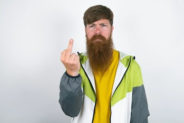 red haired man wearing sportswear standing over white studio background shows middle finger bad sign asks not to bother. Provocation and rude attitude.