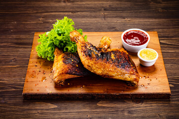 Barbecued chicken thighs with lettuce and ketchup on wooden table
