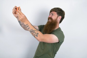 red haired man wearing green T-shirt over white studio background taking a selfie to post it on...