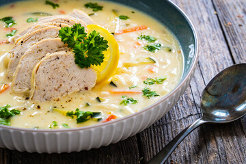 Greek lemon creamy soup with cooked chicken breast on wooden table

