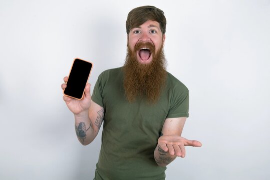 red haired man wearing green T-shirt over white studio background with a mobile. presenting smartphone. Advertisement concept.