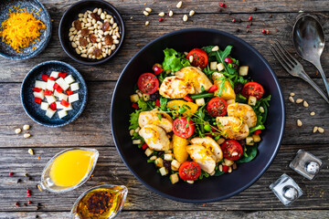 Tasty Greek salad - fried chicken breast, halloumi cheese, oranges, pine nuts, raisins, mini tomatoes and fresh green vegetables on wooden background
