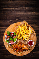 Roast chicken breast, French fries, fried mushrooms and fresh vegetables on wooden table
