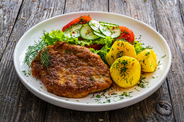 Breaded fried pork chop with fresh vegetable salad and potatoes on wooden table
