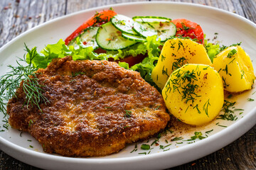 Breaded fried pork chop with fresh vegetable salad and potatoes on wooden table

