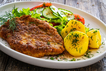 Breaded fried pork chop with fresh vegetable salad and potatoes on wooden table
