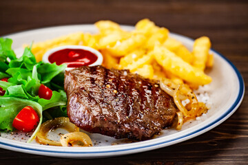 Barbecue beef steak french fries and vegetables on wooden table
