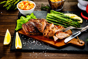 Barbecued pork french fries asparagus and vegetables on black stone plate
