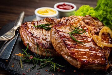 Fried beef sirloin with lettuce, ketchup and mustard on black stone plate on wooden table

