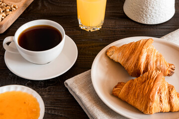 Coffee cup with croissant on a rustic dark wooden table. Food series. Two tasty fresh croissants, jam, orange juice. Continental breakfast served with freshly baked pastry. Close up view, Good morning
