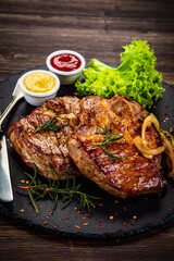 Fried beef sirloin with lettuce, ketchup and mustard on black stone plate on wooden table

